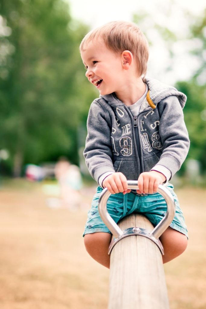 prescolar de trei ani se da pe balansoar in parc si rade