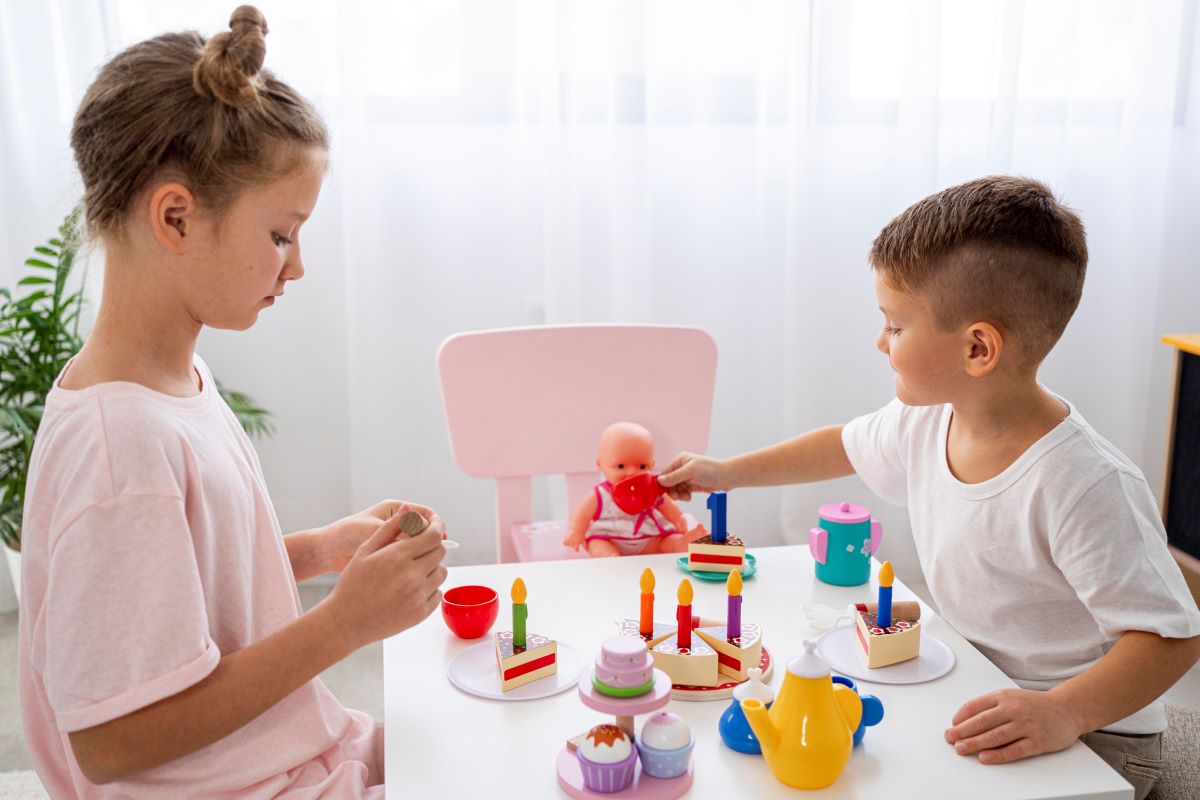 fetita si baietel care joaca un joc de rol de-a mama si de-a tata care au un bebelus a carui zi de nastere e sarbatorita